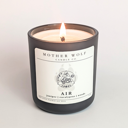 Lit candle from Mother Wolf Candle Co. with a label on a light gray background